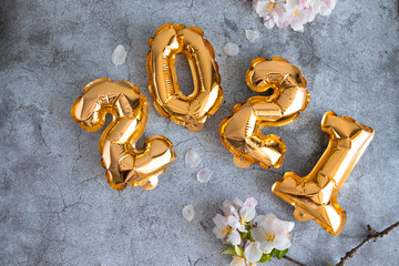 Gold 2021 balloons numbers and apple tree branches on a concrete background