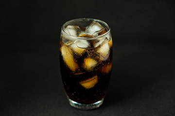 A cool glass of cola drink with ice, bubbles and fizz. Cola in glass with ice cubes isolated on dark background.