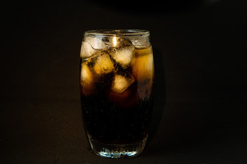 A cool glass of cola drink with ice, bubbles and fizz. Cola in glass with ice cubes isolated on dark background.