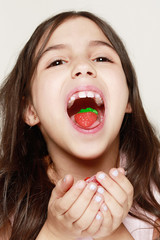 retrato de muy cerca de niña mostrardo una gominola de fresa que tiene en la boca apoyada en su...