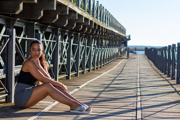 young woman sitting or standing next to a wooden and iron bridge