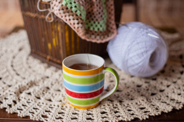 Caneca colorida com chá, sobre a mesa com novelo de linha branca e crochê ao fundo.