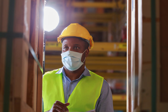 Young Black African Worker Wearing Protective Face Mask Working In Factory Warehouse. Black Man Checking Stock, New Normal After Covid 19 Pandemic Crisis. Logistic Industry Concept.