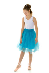 Cute little girl in a tutu and pointe shoes dancing in the studio on a white background.