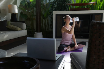 Fototapeta na wymiar Young woman drinking water after daily yoga routine at home. Healthy lifestyle concept.