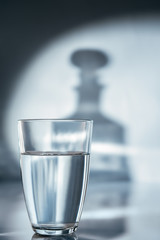 A glass of water on a blue background and a shadow from a decanter