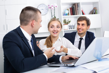 Three young business male and female assistants in formalwear having a conversation in firm office