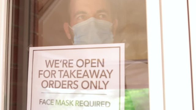 Business owner with gloves and face mask hanging an open sign "We're open for takeaway order only" at a restaurant. Concept of new normality due to coronavirus pandemic
