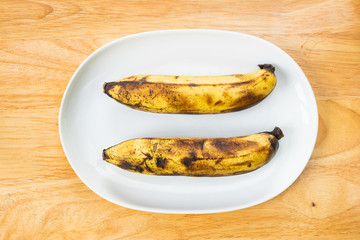 Two ripe bananas in white dish on the wooden table.