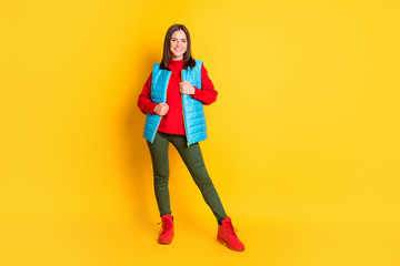 Full length photo of cute lovely young stunning lady smiling posing zipping jacket cold windy weather wear green pants blue vest red sweater boots isolated bright yellow color background