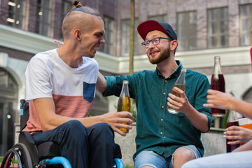 Beer time. Two friends taking a stroll on city's street in summer day. Handicapped man with his...