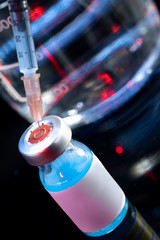 Vaccine bottle and taking the vaccine from it with a syringe on a laboratory like background.