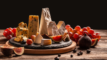 Delicious gourmet cheese, assortment of soft cheeses served with sliced sweet fresh figs and grapes on a rustic wooden background, catering, banner, menu, recipe, place for text