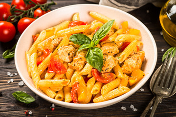 Pasta with chicken and vegetables at wooden table.