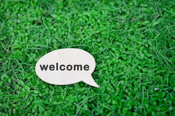 Black speech bubble with text WELCOME on grass background.