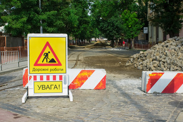Inner city road closed by stone roadblocks during reconstruction. Yellow roadsign with the words in...