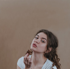 Pretty girl eating chocolate. Portrait on brown background, delicious food, sweet chocolate