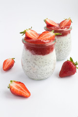 Pudding with chia and strawberry in the two glass jars on the white surface