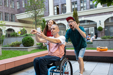 Selfie time. Group of friends taking a stroll on city's street in summer day. Handicapped man with...