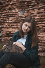 A girl in a green shirt is sitting in the garden with a rabbit on her lap against the background of a woodpile.