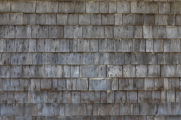 A shingled wooden wall with straight rectangular pattern. The wood is already weathered which gives the picture this old and used look.