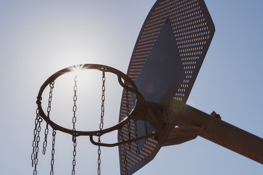 High contrast black and white image of basketball hoop backlit with sun flare