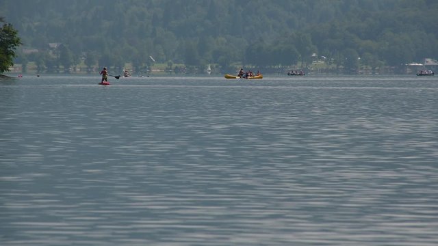 People enjoying on kayaks and sups on Bohinj lake in Slovenia. Summer season in Alpine lake. Low angle, long static shot