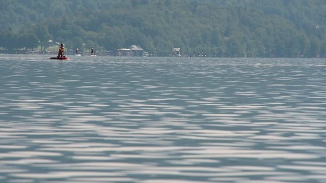 People enjoying on kayaks and sups on Bohinj lake in Slovenia. Summer season in Alpine lake. Low angle, long static shot