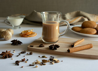 Obraz na płótnie Canvas Traditional Indian masala tea with spices. Anise, star anise, cinnamon, pepper, milk, biscuits. White and gray background.