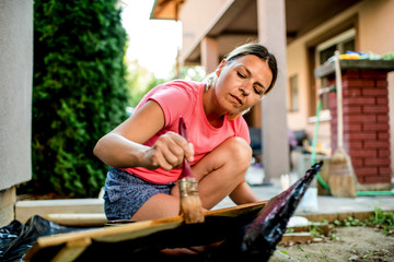 Fototapeta na wymiar Young woman painting wooden fence in backyard,