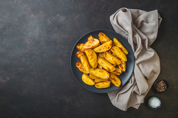 Baked potato wedges with cheese and herbs on black background