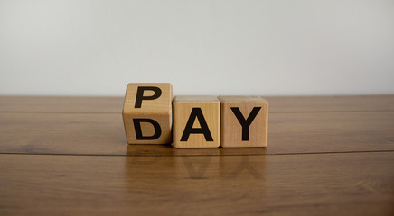Naklejka premium Turned a cube and changed the word 'Pay' to 'Day'. Beautiful wooden table. White background. Business concept.