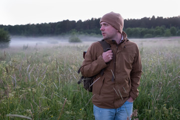 Man walking in a misty meadow hiking in the evening turning back.