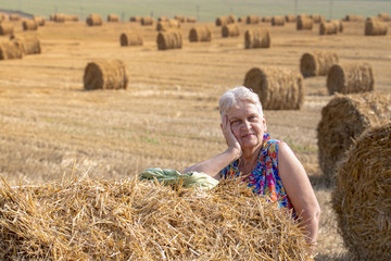 Naklejka na ściany i meble Happy active senior woman enjoying sunlight at the field with bales of straw. Authentic farm series.