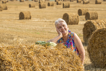 Naklejka na ściany i meble Happy active senior woman enjoying sunlight at the field with bales of straw. Authentic farm series.