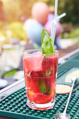 Refreshing summer non alcoholic drink cocktail with ice. Cocktail with ice in a glass with straws. Cocktail with Basil on a green table against the background of nature. Outdoor party