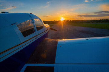 Close-up of a small parked plane with a propeller against the backdrop of a sunset.