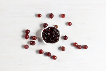 gooseberry jam in plate and fresh berries on white wooden background