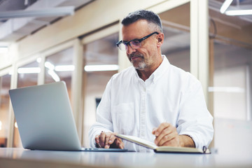 Matured business man searching information on laptop computer reading financial news.Professional lawyer in eyeglasses doing remote work concentrated while doing transaction money online on website