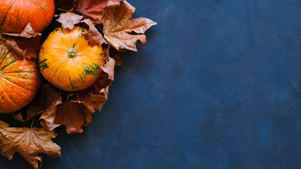Pumpkins and autumn maple leaves on dark blue background. Thanksgiving day concept. 16x9 banner,...