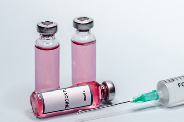 Syringe with a needle and a dose of vaccine inside. Vaccine in glass bottles on a white background.