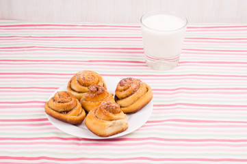 Freshly baked homemade snail buns with sugar and cinnamon on white plate and striped tablecloth with milk in glass. Balanced nutrition, proteins and carbohydrates, cereals