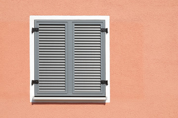 Fototapeta na wymiar Window with closed shutters on a red wall on a sunny day, space for text, 