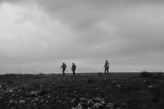black and white photo with three people in silhouette doing sport trekking can be seen in miniature on a landscape of earth and sky Italian men and women in the rural walk