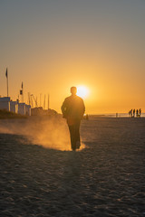 Langrune Sur Mer, France - 08 04 2020: A woman walking on the beach at sunset, with a trail of sand dust