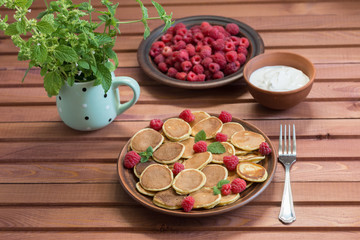 Pancake cereals and red ripe fresh raspberries in a brown plate. A bunch of Melissa in a mug on a wooden table. Delicious Breakfast
