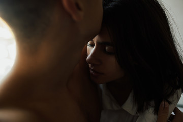 A close up portrait of two lovers hugging. Lovely girl with closed eyes kissed by her boyfriend on the forehead.