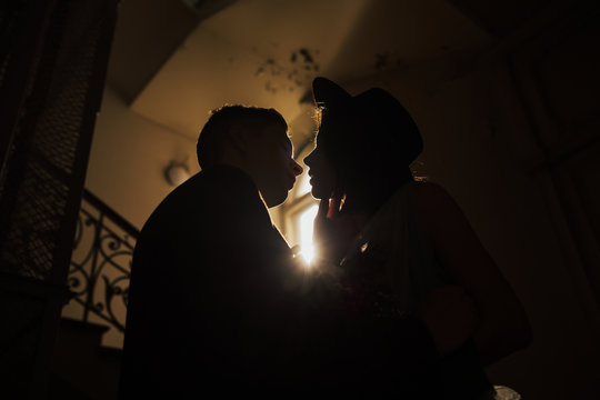 Close up portrait of happy couple of lovers standing near the window. Silhouette of a husband and wife who kiss and between them a sunbeams. 