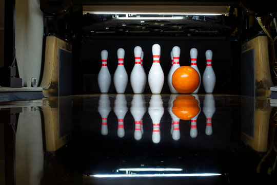 White bowling pins and an orange ball on a bowling alley. reflection