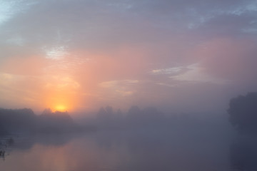 Tranquil morning landscape  at sunrise. Heavy fog over the river. Dawn illuminates and makes the clouds colorful.